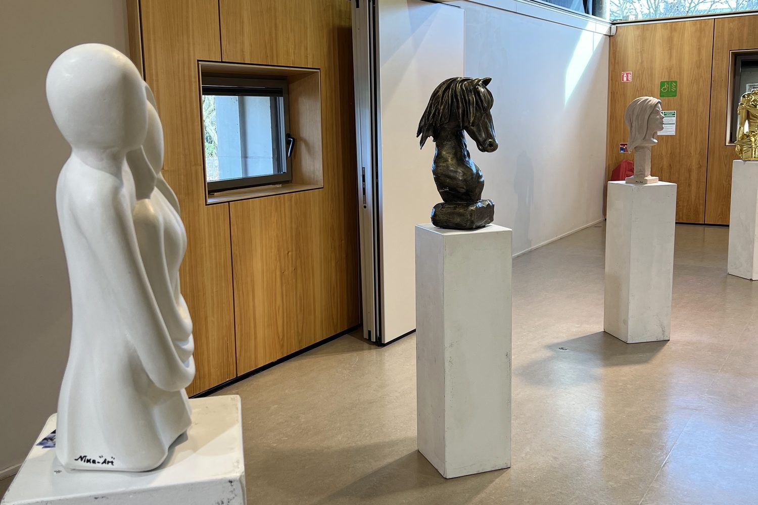 Sculpture blanche au premier plan et tête de cheval sur socle, salle de l'exposition