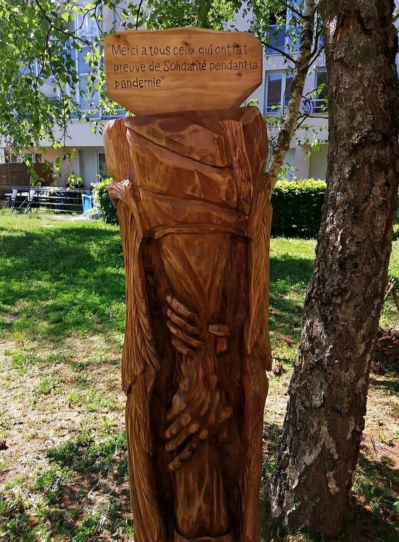 Totem sculpté dans le bois, coiffé d'une plaque gravée, dans un parc